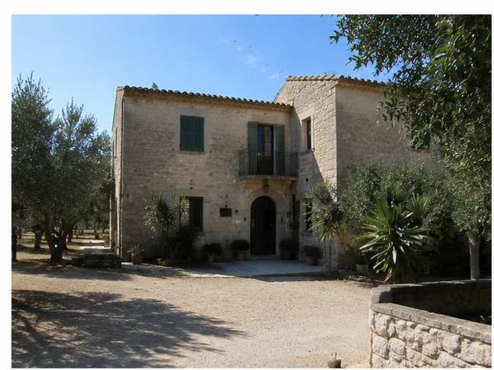 Stone exterior facade of a Sicilian country home with green shutters and olive trees